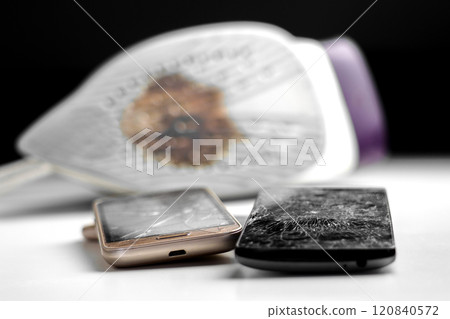 Old damaged smartphones with shattered cracked touch screens on a repair shop white table. Burned household steam electric iron blurs in the background. Black backdrop. Close up 120840572