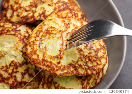 Freshly cooked fritters made with grated zucchini, almond milk, eggs and psyllium. A silver fork rests on the golden crispy surface. Close up 120840574