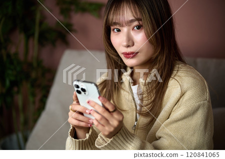 Young brown-haired woman operating a smartphone in the room Young brown-haired woman operating a smartphone in the room 120841065