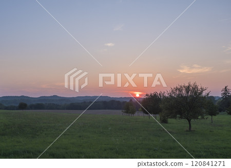 Red and pink sunset over green summer meadow and forest with deciduous tree alley, clear sky background, Countryside landscape, copy space, Kokorin region, central Bohemia 120841271