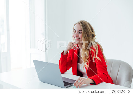 blonde woman in red business suit with laptop online in office at desk 120842060