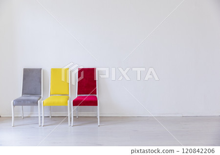 Three multicolored chairs in the interior of an empty white room Three multicolored chairs in the interior of an empty white room 120842206