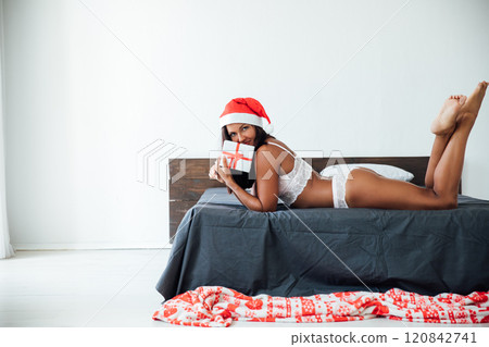 woman in lingerie on bed in bedroom near christmas tree with gifts 120842741