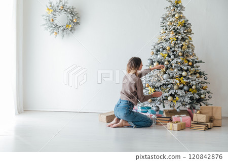 woman at decorated christmas tree with gifts, toys, lights, garlands for new year 120842876