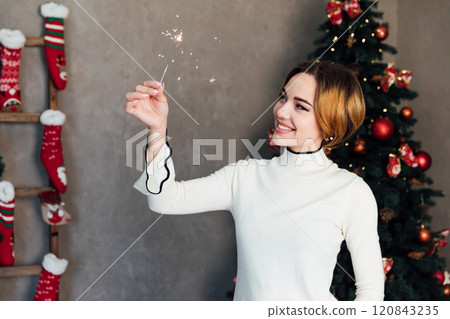Beautiful woman smiling with sparklers at christmas tree with gifts 120843235
