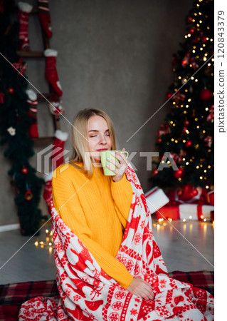 blonde woman drinking hot tea coffee at christmas tree with gifts for new year 120843379
