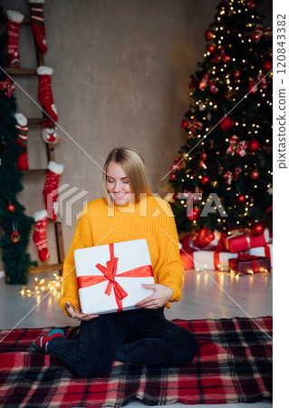 Beautiful woman smiling and opening gifts at Christmas tree for new year Beautiful woman smiling and opening gifts at Christmas tree for new year 120843382