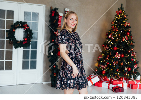 Beautiful blonde woman smiling at Christmas tree with gifts for new year Beautiful blonde woman smiling at Christmas tree with gifts for new year 120843385