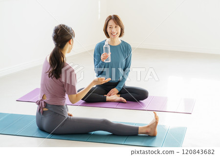 一名年輕女子和一名中年女子坐在瑜珈墊上喝水 120843682