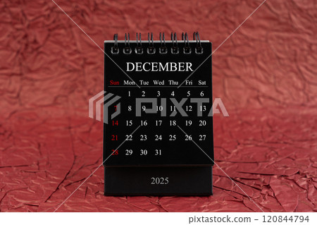 December 2025, Front view black desk calendar on crumpled red paper. 120844794