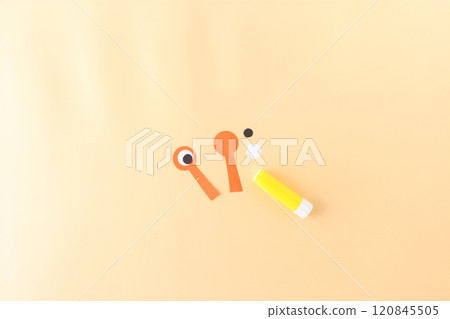 a yellow glue stick and orange paper cutout. part of a craft project, creating a character or object with eyes. a white circle and a black circle, to be used as eyes for the craft 120845505