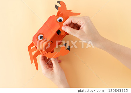 DIY crab craft made from orange painted egg carton with paper claws and eyes on a peach background. Handmade decoration project 120845515