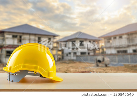 Yellow safety construction helmet on wood table with construction site background 120845540