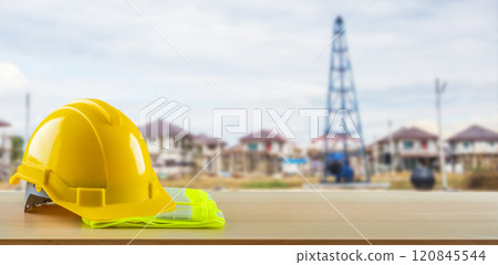 Yellow safety construction helmet on wood table with construction site background Yellow safety construction helmet on wood table with construction site background 120845544