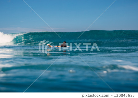 Surfer woman paddling on surfboard in ocean with crashing surfing wave. Surfer woman paddling on surfboard in ocean with crashing surfing wave. 120845653