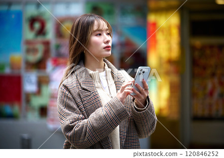 Young woman in winter clothes holding a smartphone Young woman in winter clothes holding a smartphone 120846252