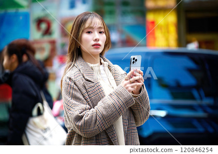 Young woman in winter clothes holding a smartphone Young woman in winter clothes holding a smartphone 120846254