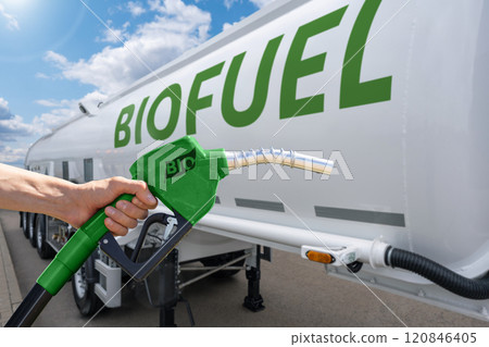 Hand with fuel nozzle with inscription BIO on a background of tank trailer with biofuel. Carbon neutral bio fuel decarbonization concept. Hand with fuel nozzle with inscription BIO on a background of tank trailer with biofuel. Carbon neutral bio fuel decarbonization concept. 120846405