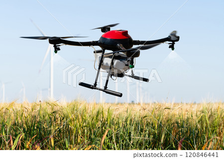 Drone sprayer flies over the agricultural field. Wind turbines on a horizon.Drone sprayer flies over the agricultural field. Wind turbines on a horizon 120846441