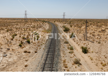 Expansive view of a winding railway through arid desert landscape with power lines nearby. Uzbekistan Expansive view of a winding railway through arid desert landscape with power lines nearby. Uzbekistan 120846788