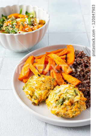 A healthy and filling meal of brown rice, baked sweet potato and squash chickpea pancakes, packed with flavor and nutrients, fresh salad of tomatoes and cucumbers 120847983