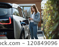 Focused Woman Checking Phone While Charging Car 120849096