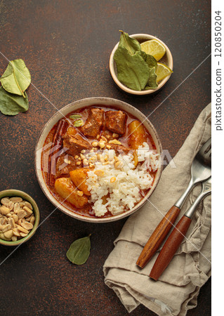 Delicious massaman curry with beef, potatoes, rice, and peanuts is served in bowl top view, Thai cuisine 120850204