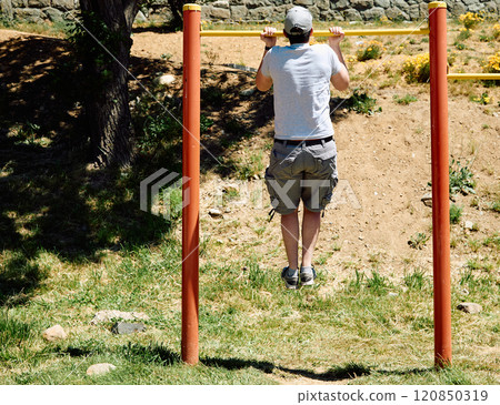 Young guy doing pull-ups on a bar in a park Young guy doing pull-ups on a bar in a park 120850319
