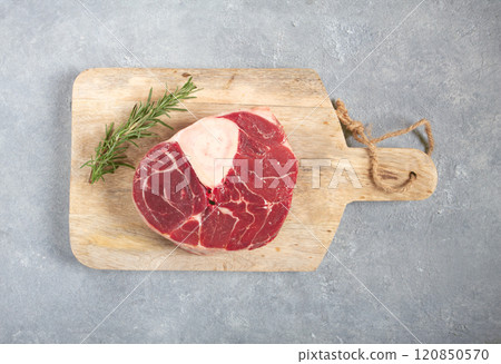 a shank on the bone, raw meat for ossobuco, on a wooden chopping board, with a branch of rosemary, top view, no people. 120850570