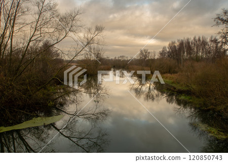 A river with trees that gives a beautiful reflection in the water. A dark sky with clouds in the background A river with trees that gives a beautiful reflection in the water. A dark sky with clouds in the background 120850743