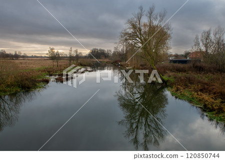 A tree gives a beautiful reflection in a river. A dark sky with clouds in the background 120850744