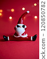 A festive Santa figurine is beautifully set against a red background with shimmering bokeh 120850782