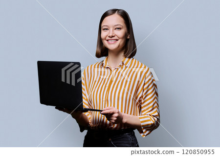 Smiling young woman with laptop on grey studio background Smiling young woman with laptop on grey studio background 120850955