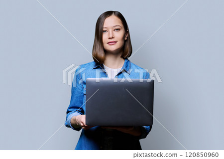 Smiling young woman with laptop on grey studio background Smiling young woman with laptop on grey studio background 120850960