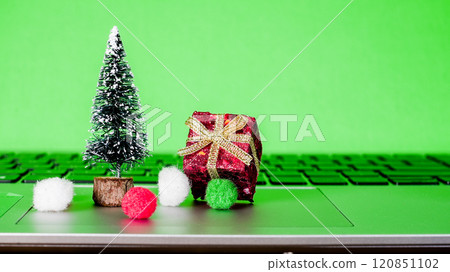 Small holiday decorations on a laptop keyboard with a green background during festive season preparations 120851102