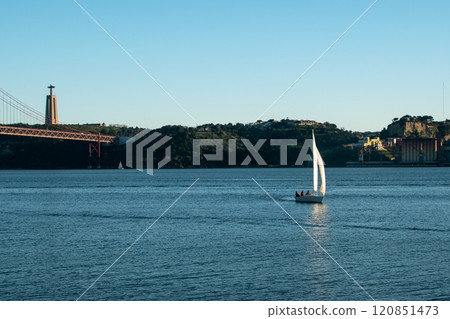 A small boat with white sails, sailboat on the river at sunset, modern architecture 120851473