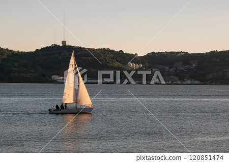 A small boat with white sails, sailboat on the river at sunset, modern architecture 120851474