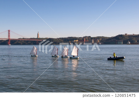 Ponte 25 de Abril Bridge and small boat with white sails, sailboat on the river at sunset, modern architecture 120851475