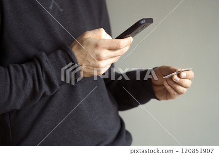 Man holds bank card and mobile phone in his hands. Man holds bank card and mobile phone in his hands. 120851907