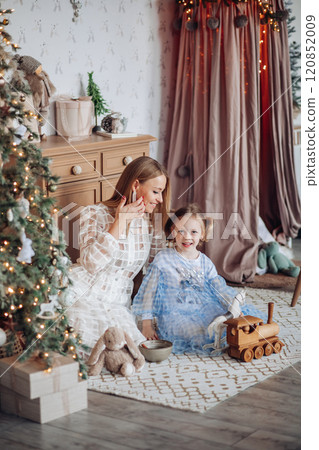 Smiling girl with mom near christmas tree at home 120852009