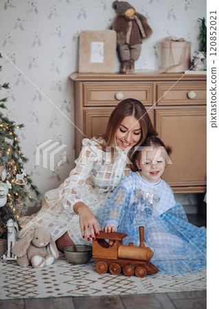 Smiling girl with mom near christmas tree at home 120852021