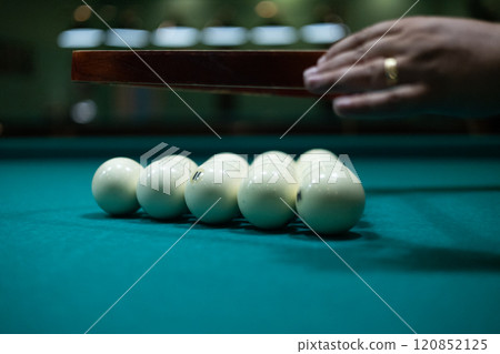 Having collected the billiard balls into a triangle, the man aligns them on the table and removes the form. Billiard pyramid filled with balls. Male hands lift a triangle from billiard balls. Having collected the billiard balls into a triangle, the man aligns them on the table and removes the form. Billiard pyramid filled with balls. Male hands lift a triangle from billiard balls. 120852125