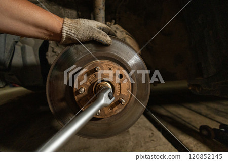 Using a wrench, a man unscrews the bolts on the car block. The driver is repairing the car in the garage. Taking care of your car and timely repairs and replacement of spare parts. 120852145