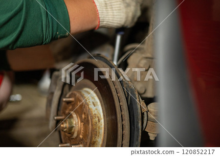 In the garage, a man is repairing a wheel on his car. A man mechanic repairs his car himself in a workshop. Concept of car repair in garage at home. 120852217
