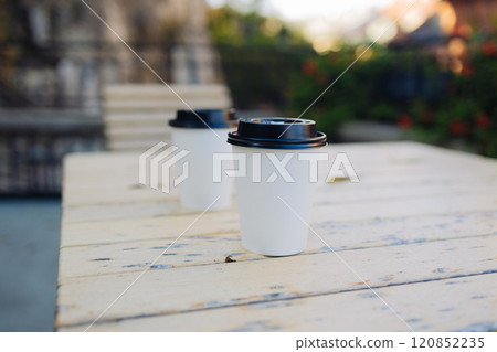 Cardboard takeaway coffee cup with plastic lid on wood table outdoors 120852235