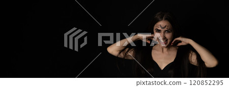 On Halloween night a witch with red nails straightens her long hair with her hands and stares piercingly into the camera. Copy space A female witch with magical symbols on her face is looking at you. On Halloween night a witch with red nails straightens her long hair with her hands and stares piercingly into the camera. Copy space A female witch with magical symbols on her face is looking at you. 120852295