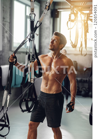 A Fit Man Engaging in Intensive Training with Suspension Equipment at the Gym Facility 120854091