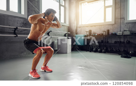 A person is squatting with a resistance band in a modern gym, highlighting their fitness journey 120854098