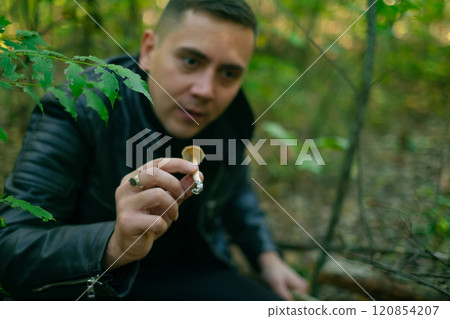 Man holding a mushroom picked in the forest during autumn mushroom harvesting season, wearing outdoor gear for foraging. 120854207