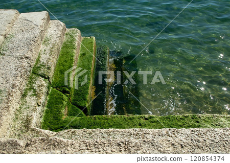 Stone staircase with green algae descending into transparent ocean waters, highlighting the texture of sea waves and a striking water-themed backdrop. Stone staircase with green algae descending into transparent ocean waters, highlighting the texture of sea waves and a striking water-themed backdrop. 120854374